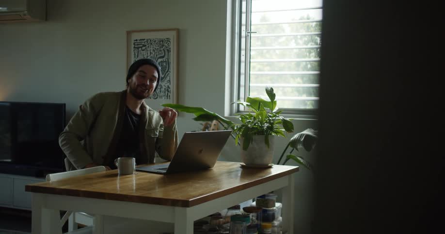 Young man laughing and talking in a video call from a laptop on a table at home