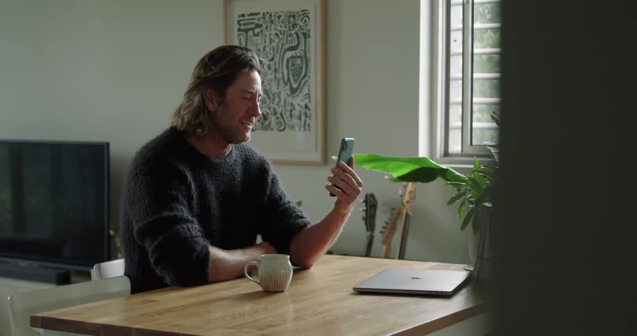 Long haired young man saying goodbye on a video call in a smartphone at home
