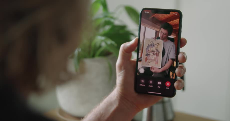 A person holds a cell phone displaying a man holding up artwork on the screen indoors