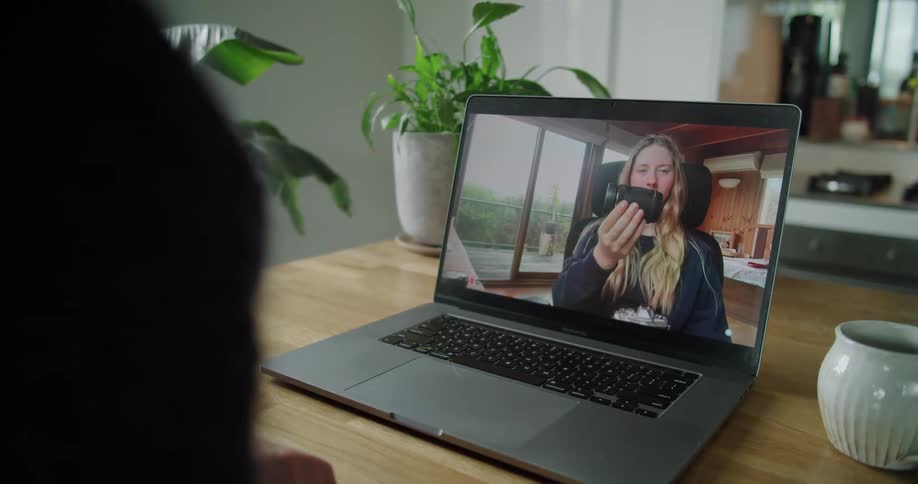 A person sits at a table having a video call on a laptop with a female