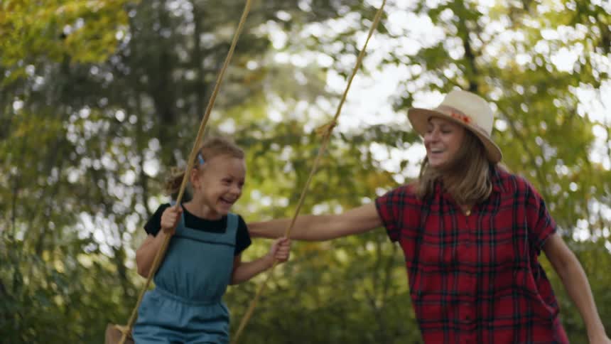 A mother pushing her daughter on a swing