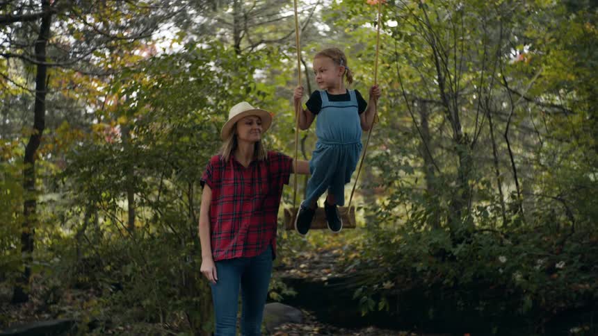 Mother pushing her daughter standing on a tree swing outdoors