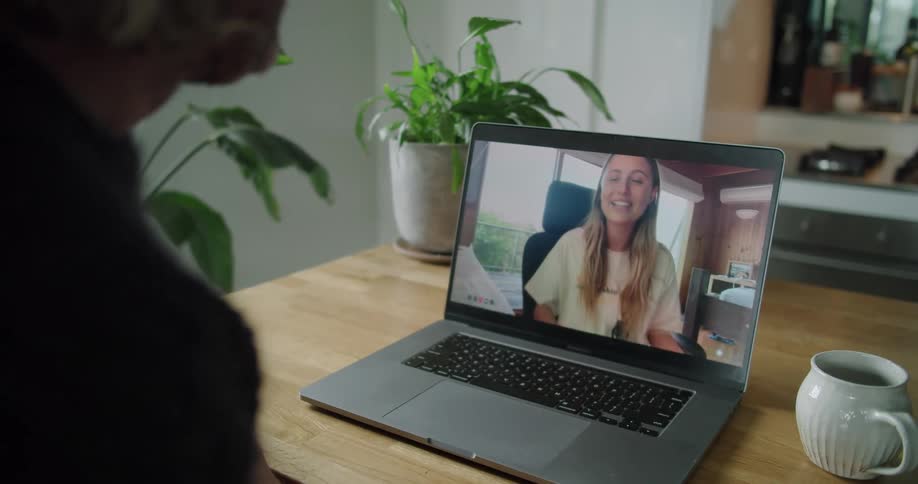 A man sitting at desk in a house participates in a videochat with a young woman on his laptop