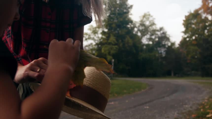Mother and daughter hanging an autumn leaf on a sun hat at sunset