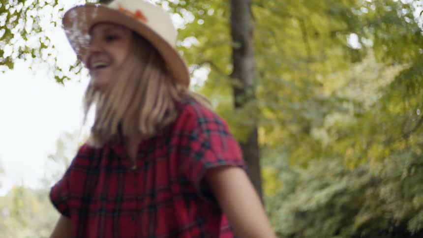 A woman in a hat and plaid shirt smiles while pushing her daughter on a swing in the park