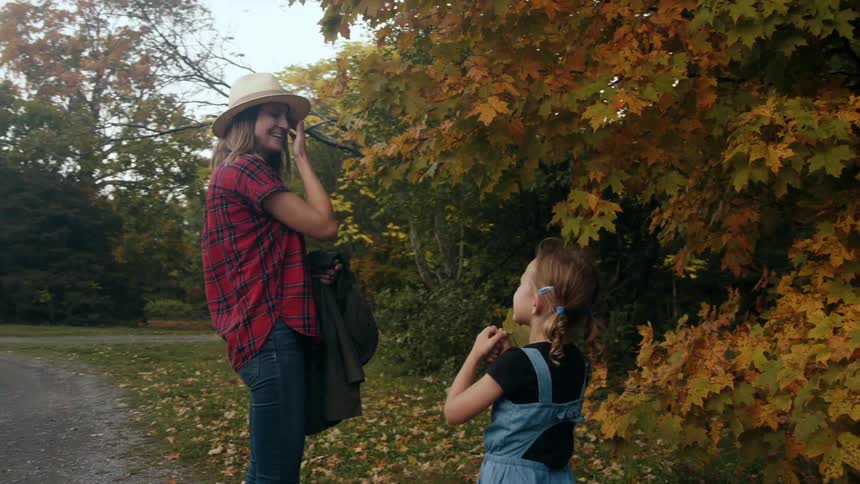 A mother and daughter outside near fall trees collecting leaves