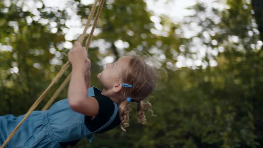 A woman pushing a little girl on a swing with trees the sky and clouds in the background