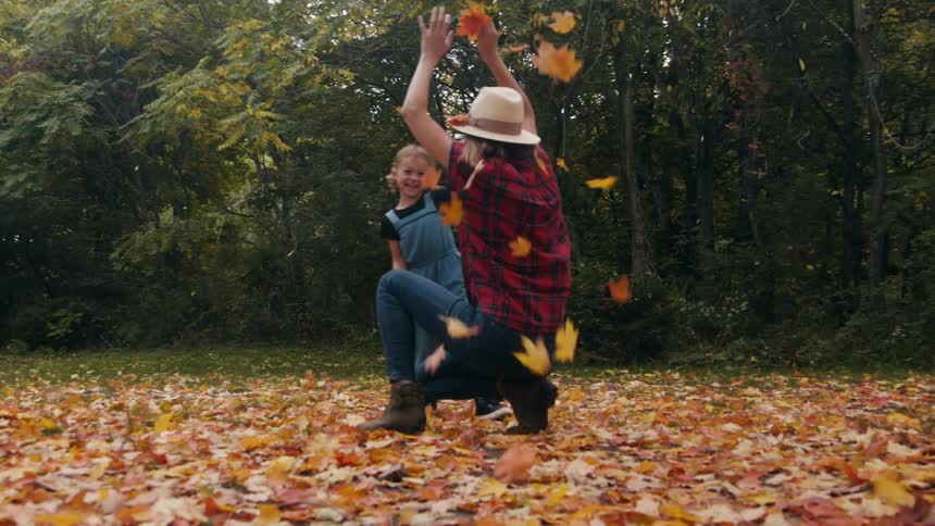 Mother and daughter playing with fall leaves in the backyard at fall