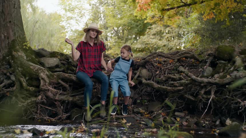 Mother and daughter throws pebbles into a small creek in the forest