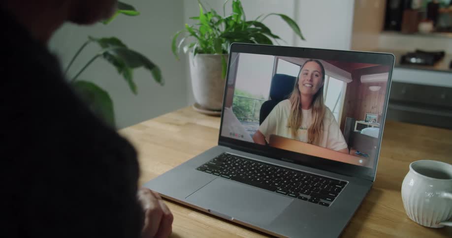 Woman talking and smiling on a laptop screen in a living room on a wooden coffee table