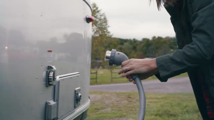 Woman wearing a sun hat plugging an electric cord to the external outlet on a caravan