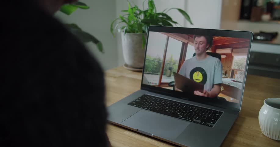 A person sits at a table having a video call with another man on a laptop