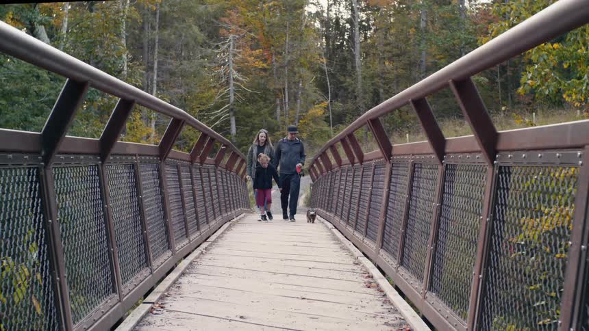 Family walking their dog across a narrow bridge in the wilderness