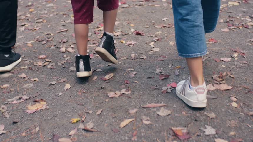 Three people walking on a gravel walkway where autumn leaves are scattered around