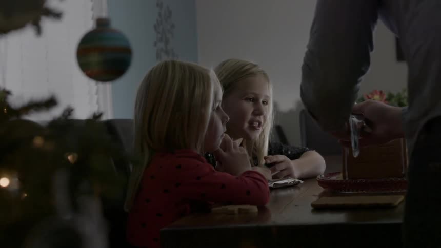 Two girls watch an adult ice a gingerbread house