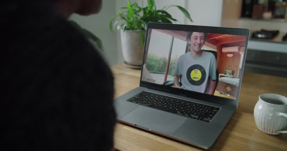 A person sits at a table having a video call on a laptop with another man