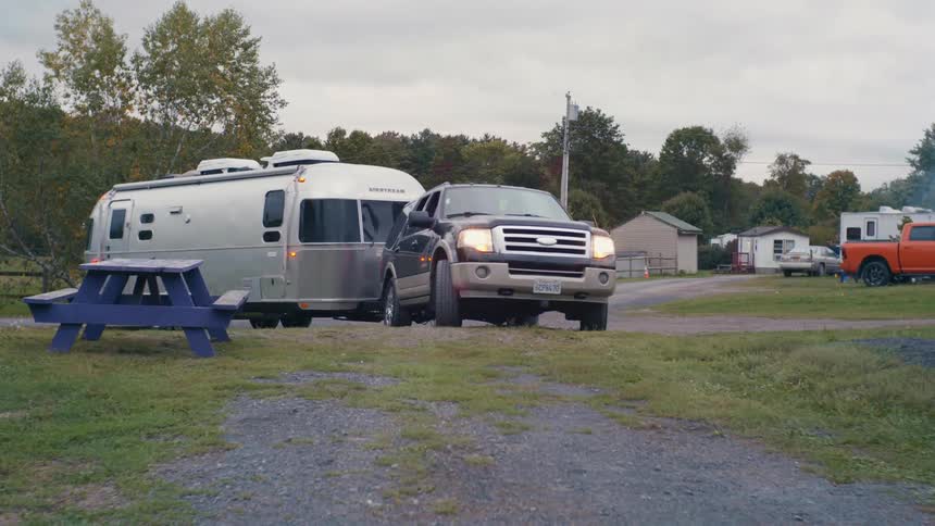 A sport utility vehicle pulls a large silver camper onto a campground