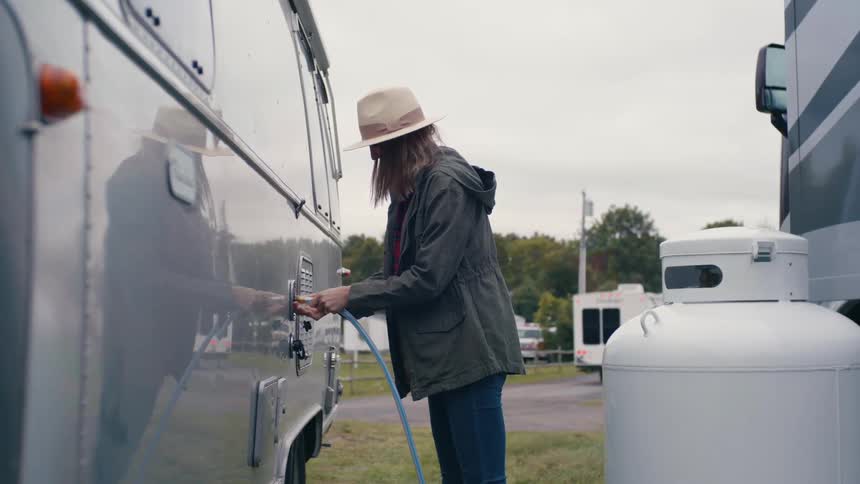 A woman using a hose on a rv vehicle filling the gas