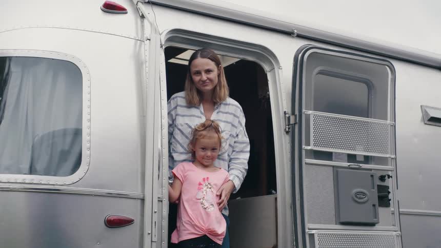 Mother and daughter standing in the doorway of a mobile home at daytime