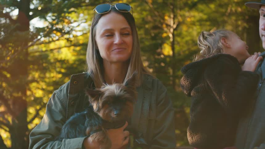 Mother holding a small brown and black yorkie standing next to her husband and daughter outside and smiling