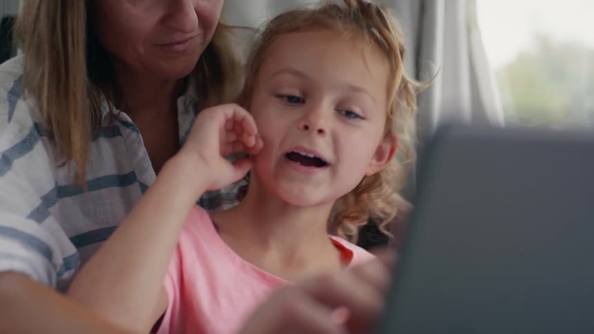 A girl sits in her mothers lap as they use a laptop and turns around to laugh and smile