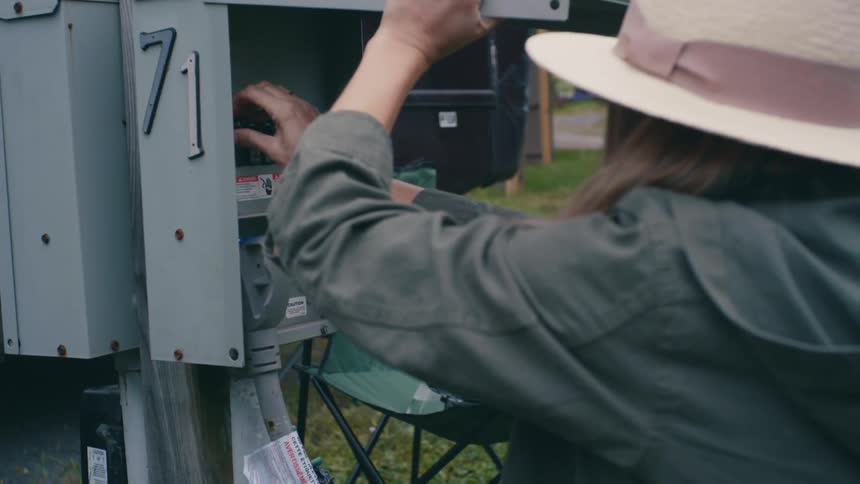 Woman wearing a sun hat plugs a caravan trailer to a power outlet in a park