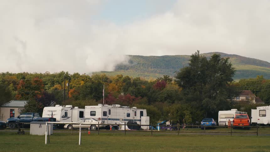 Rvs parked at a campground in the grass next to a mountain with a cloudy overcast at daytime