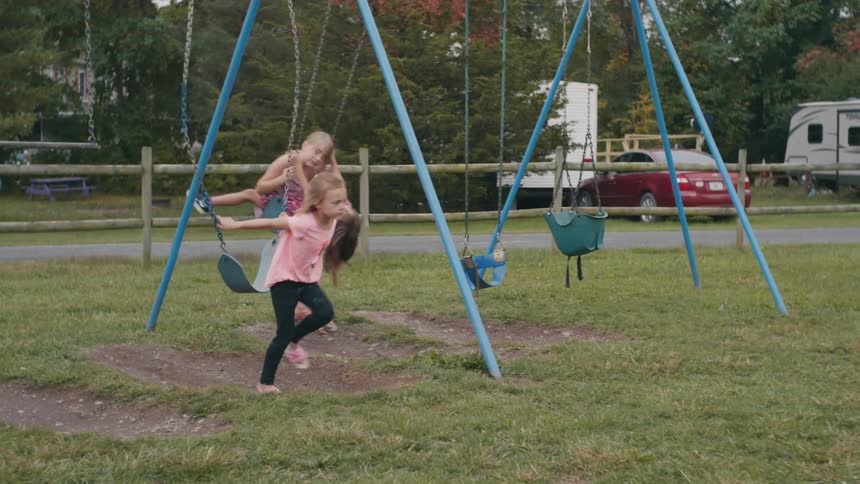 Three girls ride swings at a playground on a campground