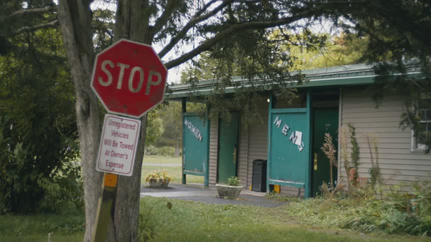Stop sign in front of a tree next to public restrooms in a park