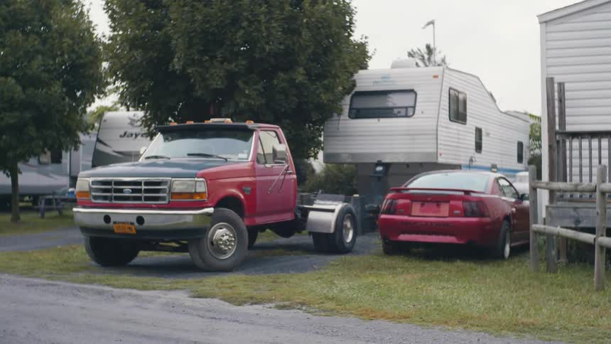 A ford truck and mustang parked next to a trailer in a park