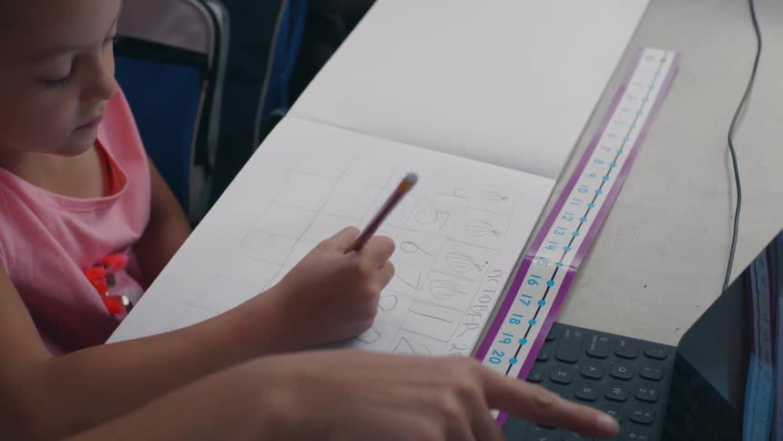 Little girl sitting down at a table in front of a tablet with a keyboard doing math homework