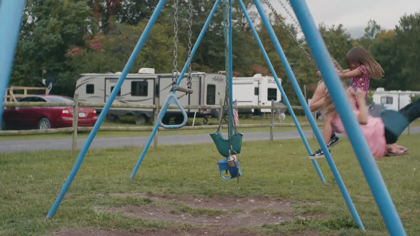 Girls playing on the swings in the playground next to the trailer park
