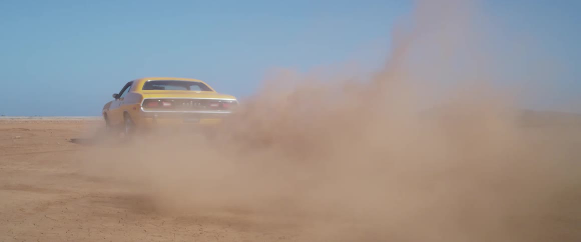 A yellow sports car accelerates and drives in the desert against a blue sky