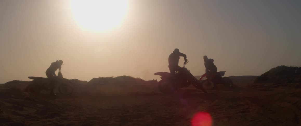Three people on dirt bikes spinning in circles out in a desert area at day time