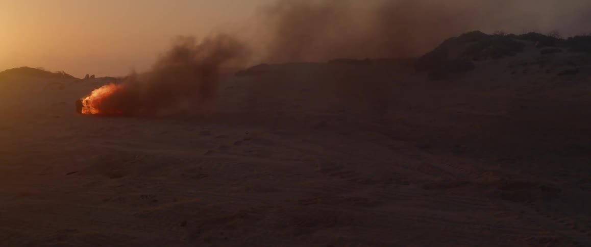 Smoke coming out of a tire on fire on the sand of a desert at sunset