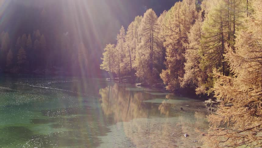 An aerial view of a lake trees and mountains with sun streaming down