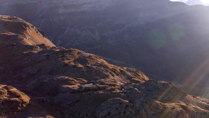 Large brown mountain range with a hiking path in a valley down below during the daytime