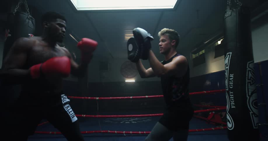 Muscular shirtless man practices full contact boxing with a sparring partner inside a gym