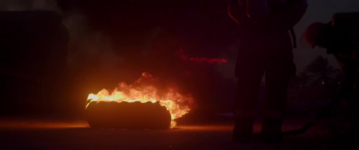 A person stands in front of an item that is on fire