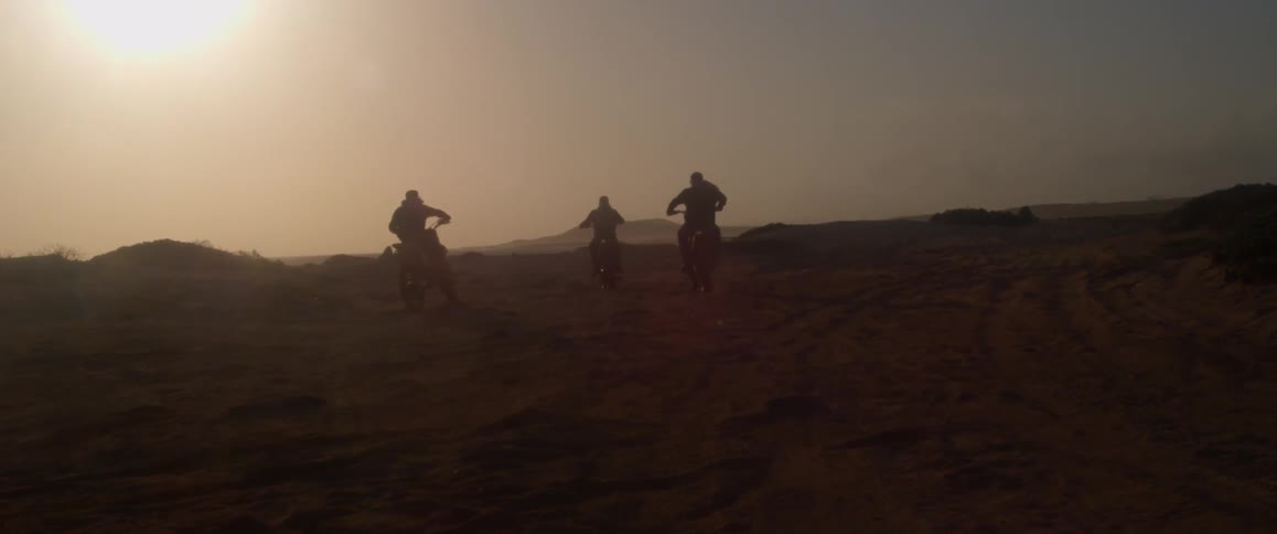 The silhouette of three riders on motor bikes as they ride with the sun glowing down