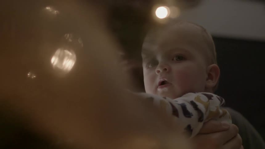 Bearded man holding his infant as they look at their christmas tree