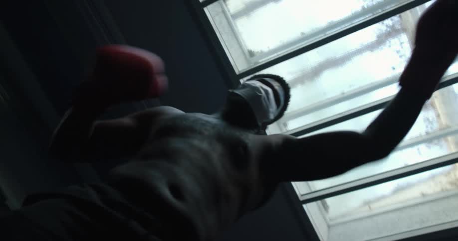 Two men are boxing while wearing gloves and a mask under a skylight indoors