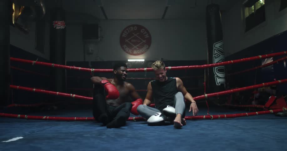 Two male boxer sit down side by side and laugh together in the boxing ring