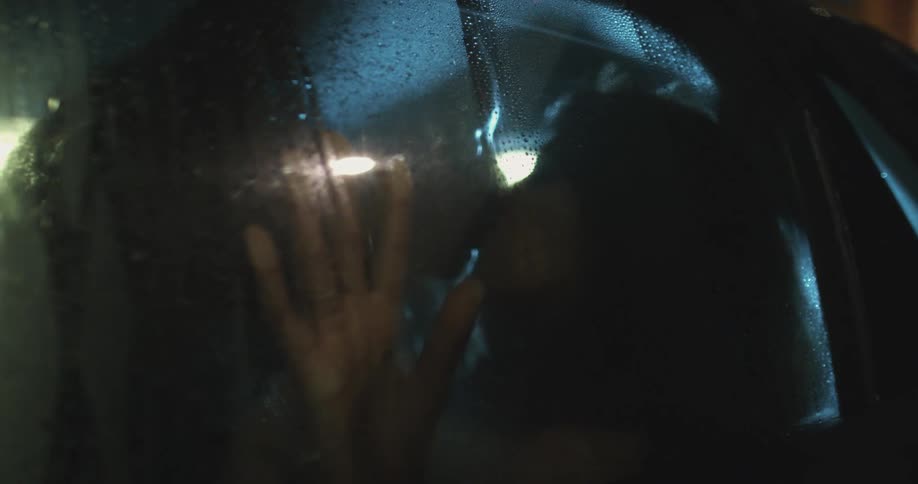 Two women kissing in the back seat of a parked car at night