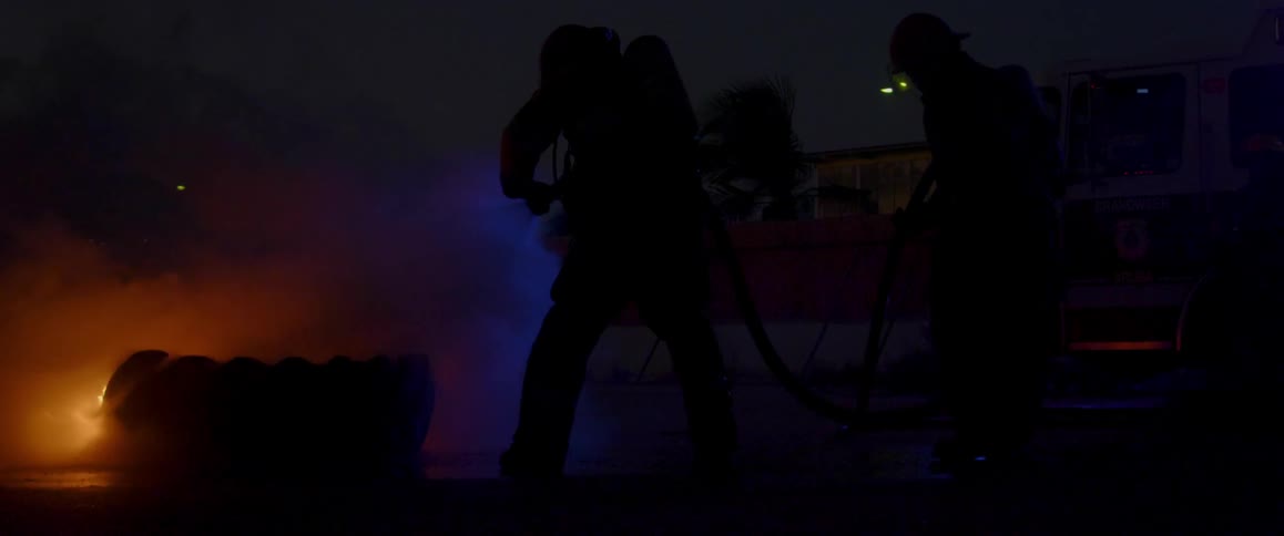 Firefighters use hoses to extinguish a tire fire outdoors at night