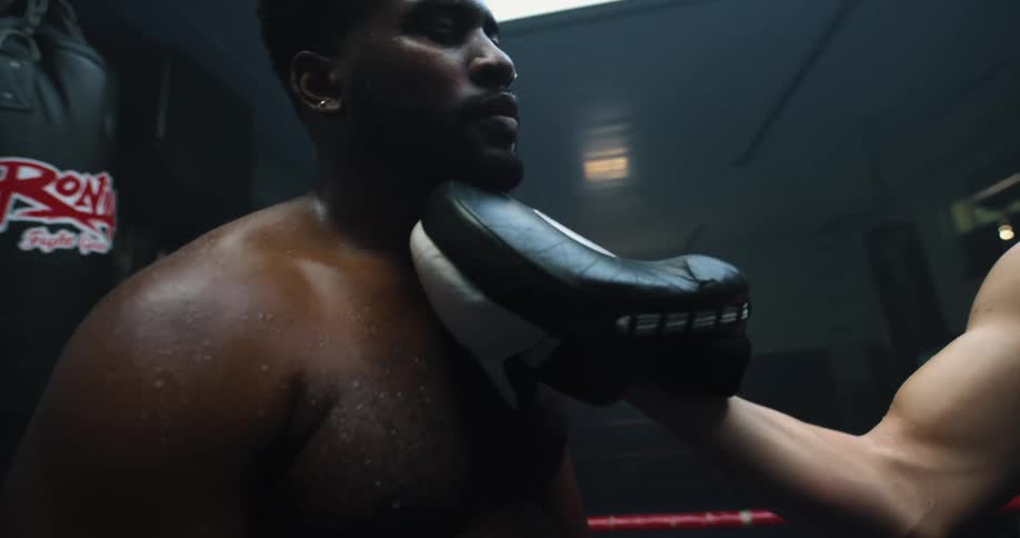A male boxer approaches another boxer aggressively while standing in a boxing ring