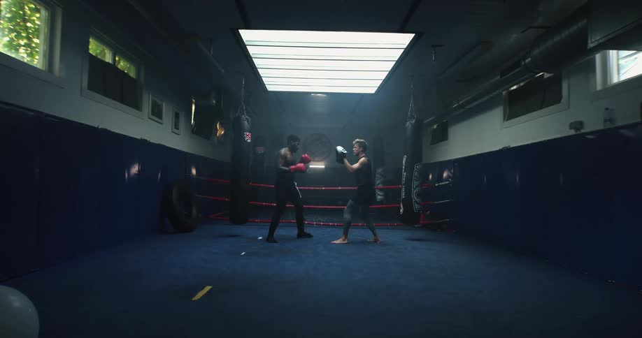Two men are sparring in a boxing facility surrounded by blue floor and walls