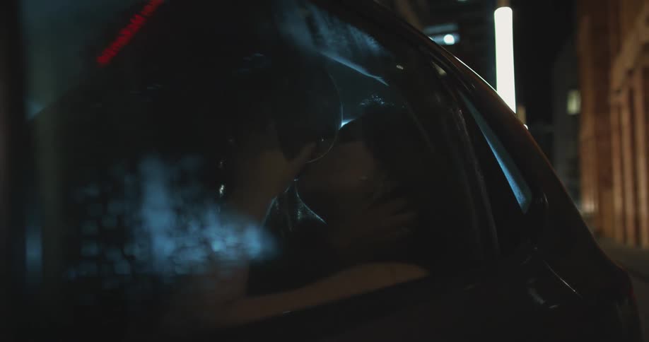 Couple passionately kissing inside a car parked in the city at night