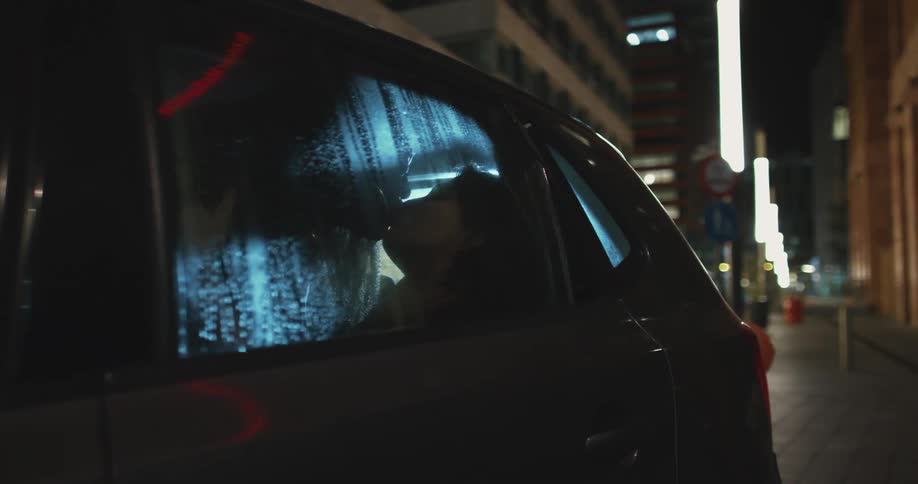 Two people kissing in the back seat of a car on a city street