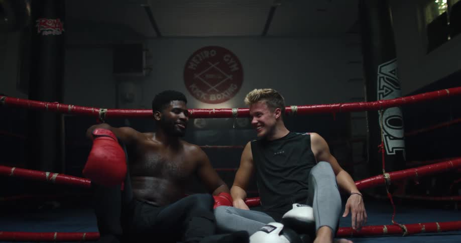 Two men sit together talking and laughing in a boxing ring